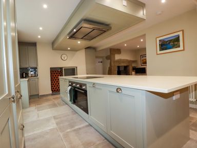A kitchen with an island featuring an oven and stovetop a clock on the wall and framed pictures at Tretoil Farm House in Bodmin