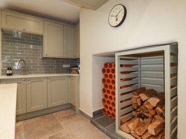 A kitchen corner with cabinets a sink and a clock above a fireplace storing wood and terracotta tubes at Tretoil Farm House in Bodmin