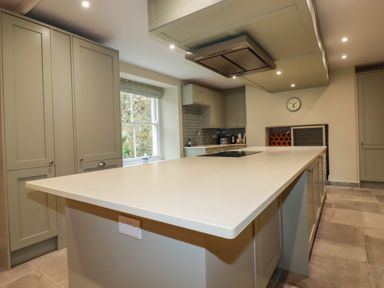 A kitchen with an island countertop cabinets and a window showing a stone wall at Tretoil Farm House in Bodmin