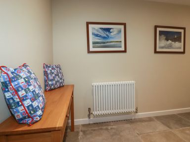 A room with a wooden bench with two patterned cushions a white radiator on the wall and two framed pictures at Tretoil Farm House in Bodmin
