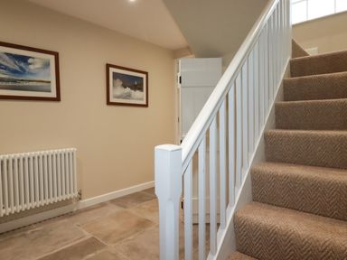 A hallway with carpeted stairs a white radiator and framed pictures on the wall at Tretoil Farm House in Bodmin