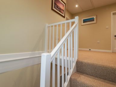 A carpeted staircase with white railing leading to a landing with framed pictures on the walls at Tretoil Farm House in Bodmin