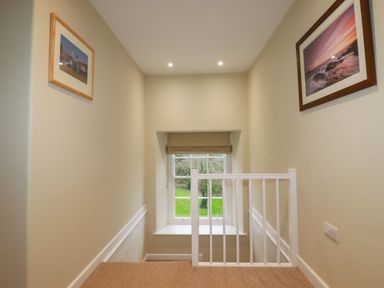 A staircase landing with a window and two framed pictures on walls at Tretoil Farm House in Bodmin