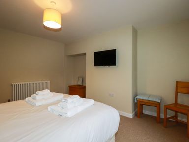 A bedroom with a bed and towels a wall mounted TV a wooden chair and a small wooden table at Tretoil Farm House in Bodmin