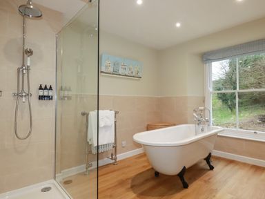 A bathroom with a clawfoot bathtub a glass-enclosed shower and a window showing outdoor greenery at Tretoil Farm House in Bodmin