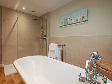 A bathroom with a white bathtub a walk-in shower a towel rack and wall art at Tretoil Farm House in Bodmin