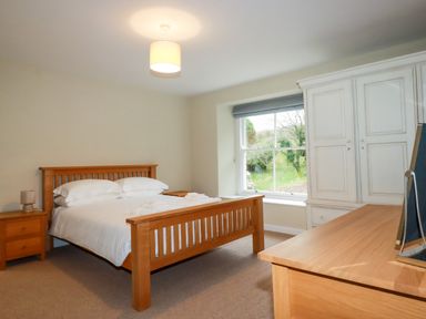 A bedroom with a wooden bed and nightstand a dresser and a white wardrobe by a window at Tretoil Farm House in Bodmin