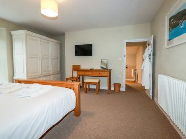 A bedroom with a wooden bed, white wardrobe, wooden desk and chair, wall-mounted tv, and an open door showing bathrobes at Tretoil Farm House Bodmin