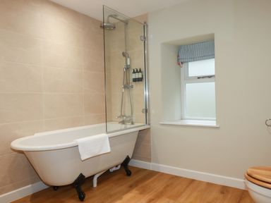A bathroom with a clawfoot bathtub shower combination and window at Tretoil Farm House in Bodmin