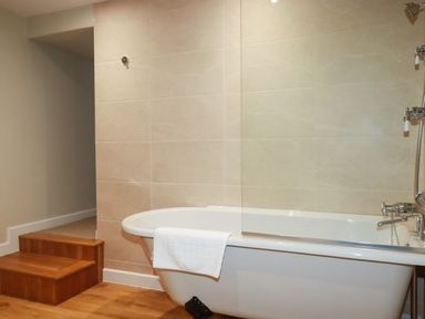 A bathroom with a white bathtub and wooden steps at Tretoil Farm House Bodmin