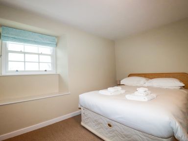 A bedroom with a bed with white linens and folded towels by a window with a blue blind at Tretoil Farm House in Bodmin