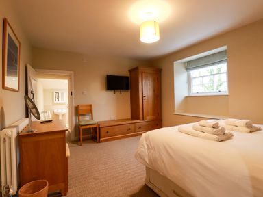 A bedroom with a bed with folded towels a wooden wardrobe a chair a wall-mounted TV and a window at Tretoil Farm House in Bodmin