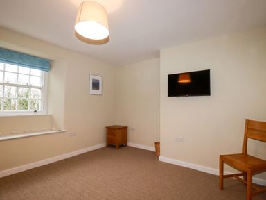 A room with a window with blue blinds a wooden chair a small wooden cabinet a wall mounted TV and a ceiling light at Tretoil Farm House in Bodmin