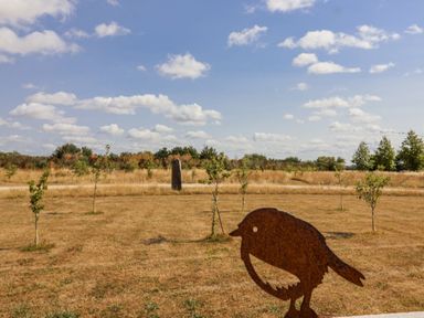 An outdoor area with grass, trees, clouds and a bird sculpture at The Little Loft in Burford