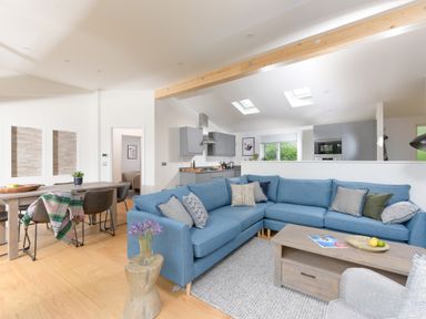 An open plan living room and kitchen with a blue sectional sofa wooden coffee table dining table and gray kitchen cabinets at 5 Southern Place in Dobwalls