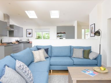 A living room with a blue sectional sofa and a wooden coffee table overlooking a kitchen with grey cabinets at 5 Southern Place in Dobwalls