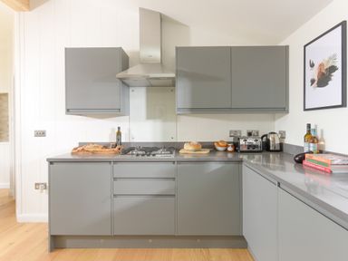 A kitchen with grey cabinets a gas stove bread on cutting boards a toaster kettle bottles and cookbooks on the counter at 5 Southern Place in Dobwalls
