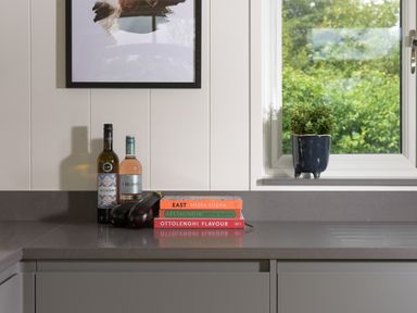 A kitchen countertop with two bottles, two eggplants, three stacked cookbooks, and a potted plant on the windowsill at 5 Southern Place in Dobwalls