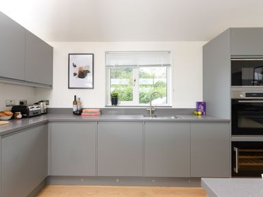 A kitchen with grey cabinets a window with blinds a sink and kitchen appliances at 5 Southern Place in Dobwalls