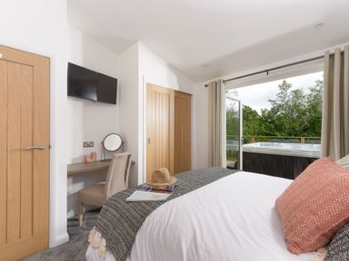 A bedroom with a bed a desk and chair a wall mounted television and a hot tub outside at 5 Southern Place in Dobwalls