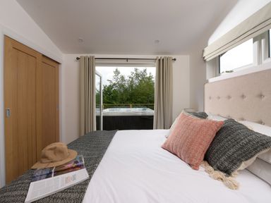 A bedroom with a bed pillows curtains and a door leading to an outdoor area with a hot tub at 5 Southern Place in Dobwalls
