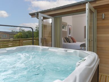 An outdoor hot tub next to a wooden deck with an open door leading to a bedroom at 5 Southern Place in Dobwalls