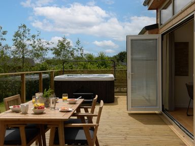 An outdoor deck with a wooden dining table set food and drinks and a hot tub at 5 Southern Place in Dobwalls