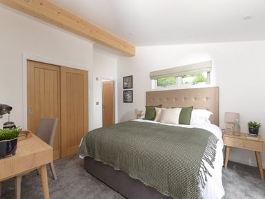 A bedroom with a bed with a beige headboard green and white bedding two wooden bedside tables with lamps and plants and a wooden desk with a chair at 5 Southern Place in Dobwalls