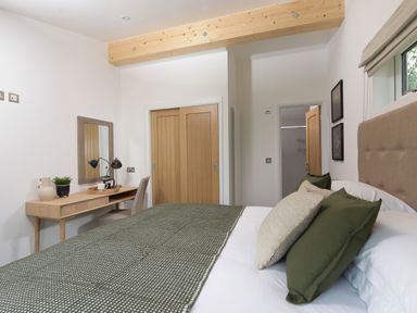 A bedroom with a bed with green and beige pillows a wooden desk with a mirror a chair sliding wooden closet doors and a wooden ceiling beam at 5 Southern Place in Dobwalls
