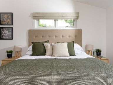 A bedroom with a bed with pillows and a green blanket two bedside tables with lamps and plants and framed pictures on the wall at 5 Southern Place in Dobwalls