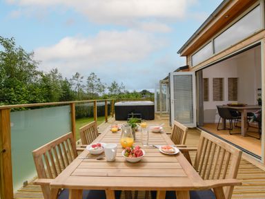 An outdoor wooden deck with a dining table and chairs set for breakfast a hot tub and greenery beyond 5 Southern Place Dobwalls