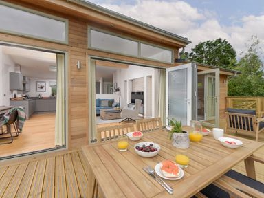 An outdoor wooden deck with a table set with food and drinks and a view into a kitchen and living room at 5 Southern Place in Dobwalls