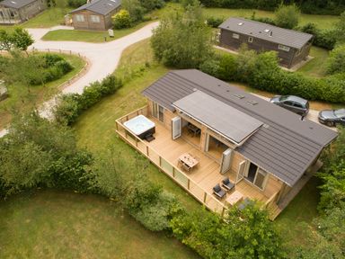 An aerial view of a wooden cabin with a deck hot tub outdoor furniture and surrounding greenery at 5 Southern Place in Dobwalls