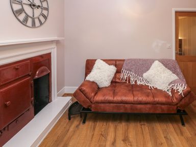 A room with a brown sofa with white cushions and a purple throw a red fireplace and a wooden floor