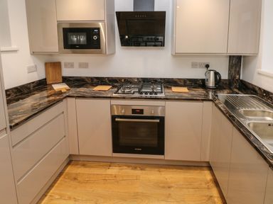 A kitchen with black marble countertops stove oven microwave kettle and sink at Swn Y Mor in Burry Port