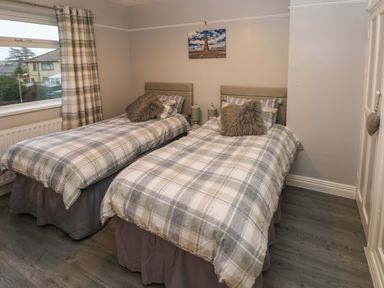 A bedroom with two single beds with plaid bedding and furry pillows at Swn Y Mor in Burry Port