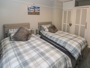 A bedroom with two single beds with checkered bedding and furry pillows at Swn Y Mor in Burry Port