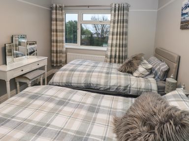 A bedroom with two single beds with plaid bedding a dressing table with mirror and a window with plaid curtains at Swn Y Mor in Burry Port