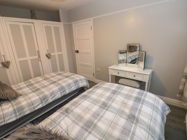 A bedroom with two single beds with plaid bedding a white dresser with mirrors and a white double-door closet at Swn Y Mor in Burry Port