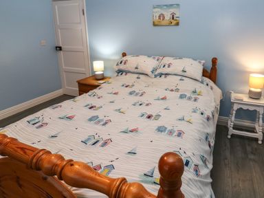 A bedroom with a wooden bed with beach-themed bedding bedside tables with lamps and a painting on the wall at Swn Y Mor in Burry Port