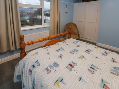 A bedroom with a wooden bed, a window with curtains, a white wardrobe, and a chair with a cover at Swn Y Mor in Burry Port