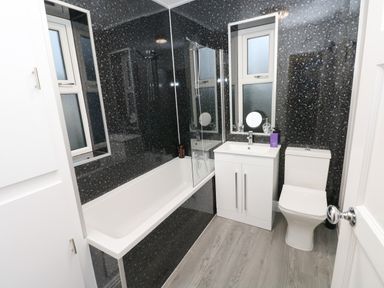 A bathroom with a bathtub shower combination a sink with cabinet a toilet and windows at Swn Y Mor in Burry Port
