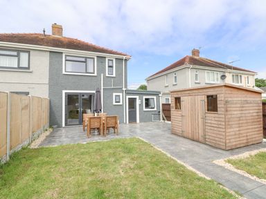 A backyard with a gray house patio wooden garden furniture and a wooden shed at Swn Y Mor in Burry Port