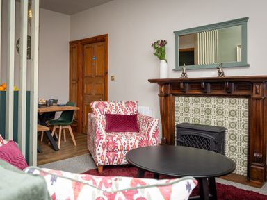 A living room with patterned armchairs a wooden fireplace and a dining table with green chairs at Watermouth Castle Bassett Apartment Berrynarbor near Ilfracombe