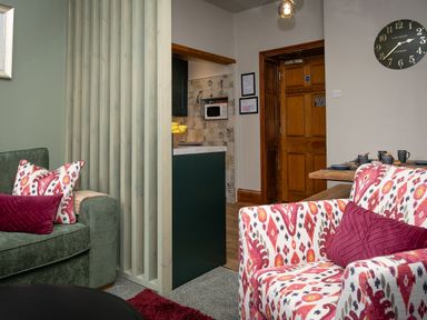 A living room with patterned armchair and green sofa near a wooden door and kitchen at Watermouth Castle Bassett Apartment Berrynarbor near Ilfracombe