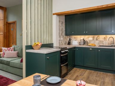 A kitchen with dark green cabinets wooden countertops and a partially visible living room at Watermouth Castle Bassett Apartment in Berrynarbor near Ilfracombe