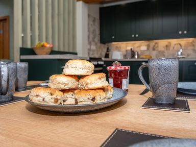 A kitchen table with a plate of scones jam and mugs in a kitchen at Watermouth Castle Bassett Apartment Berrynarbor near Ilfracombe