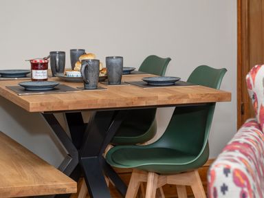 A wooden dining table with grey plates mugs and a jar of strawberry conserve with green chairs at Watermouth Castle Bassett Apartment Berrynarbor near Ilfracombe