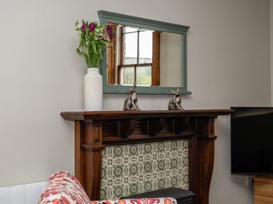 A fireplace with green patterned tiles a wooden mantle a vase with flowers two rabbit figurines and a mirror above at Watermouth Castle Bassett Apartment in Berrynarbor near Ilfracombe