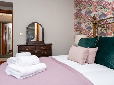 A bedroom with a bed with pillows and folded towels and a wooden dresser with a mirror at Watermouth Castle Bassett Apartment Berrynarbor near Ilfracombe